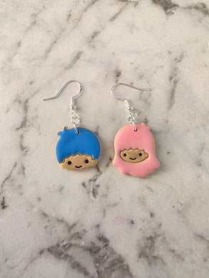 Lala and Kiki mismatched earrings – one with blue cartoon face and one with pink hooded character, handmade from polymer clay.