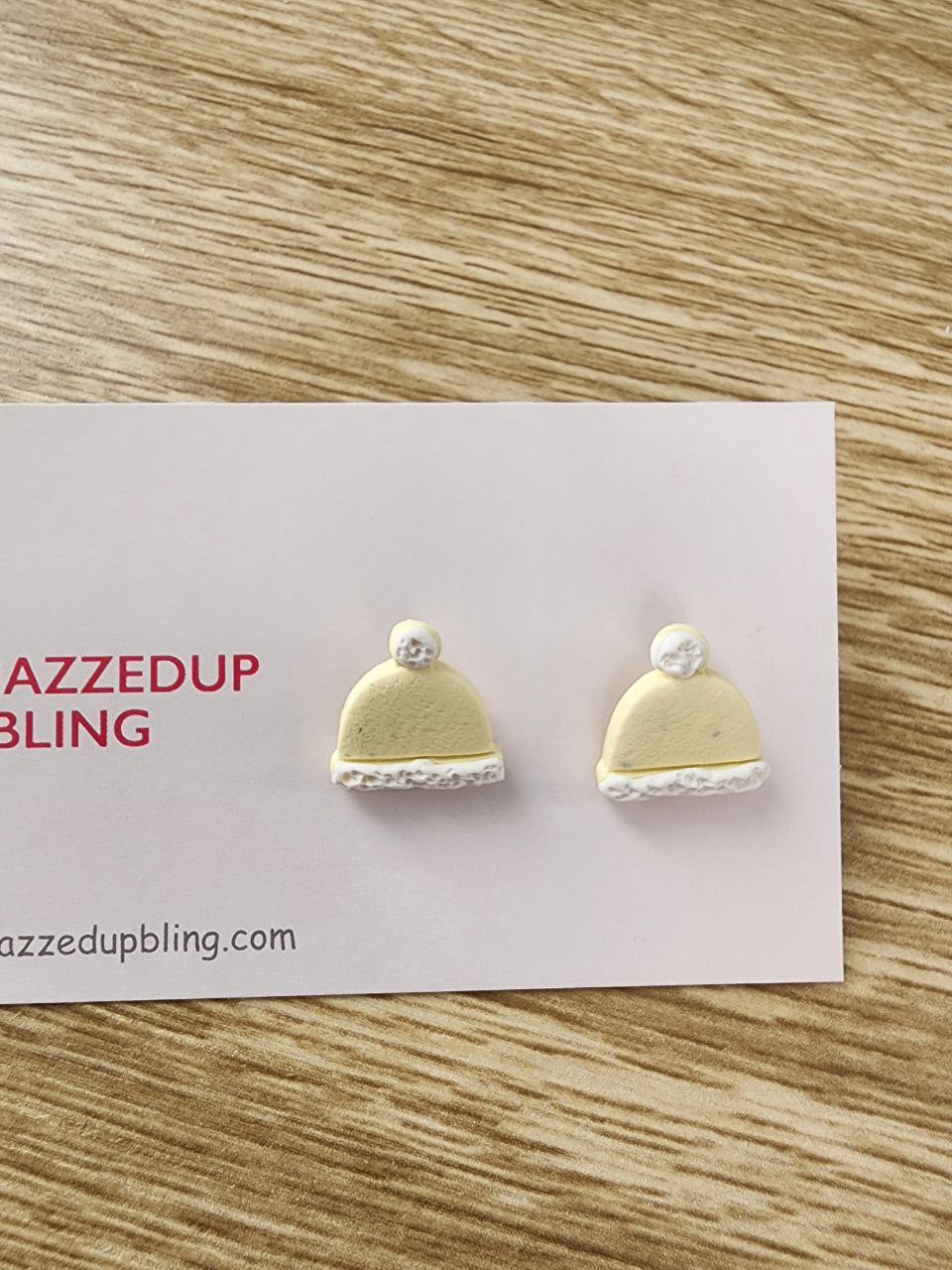 Yellow beanie-shaped polymer clay earrings with white trim and pom-poms, handmade by Jazzed Up Bling in New Zealand.