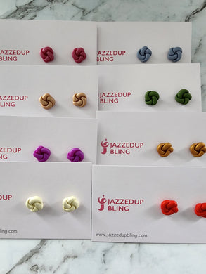 Set of eight handmade polymer clay twist knot stud earrings in assorted colours — berry pink, sky blue, beige, green, purple, caramel, cream, and red — crafted by Jazzed Up Bling in New Zealand.